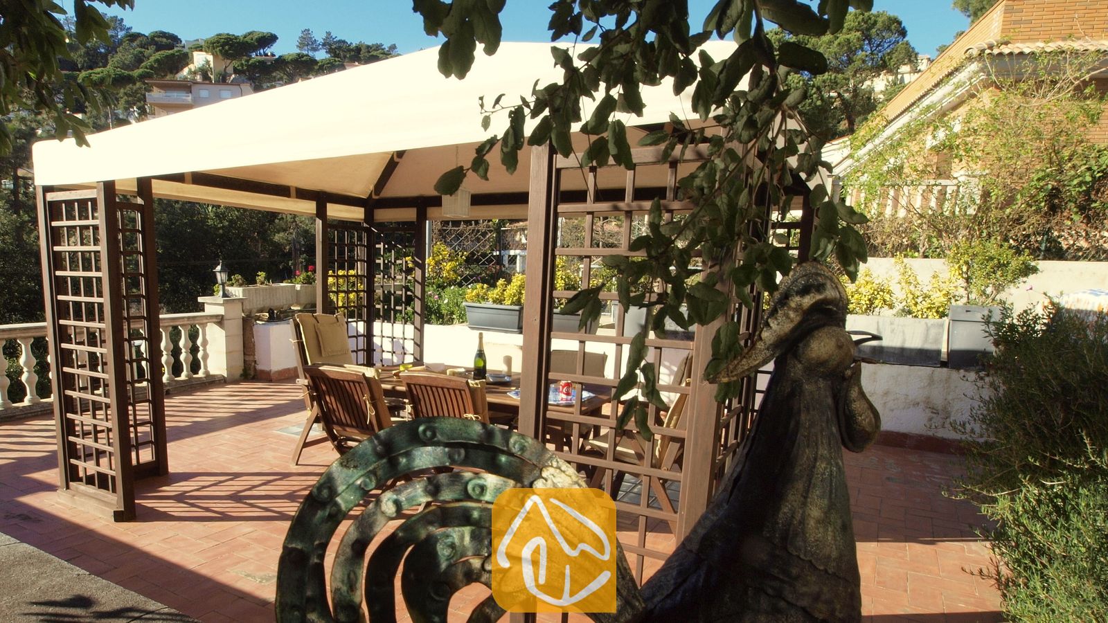 Vakantievilla's Costa Brava Spanje - Villa Noa - Houten pergola met een stoffen doek op een zonnig terras bij Villa Noa, voorzien van een eettafel en stoelen in de schaduw.