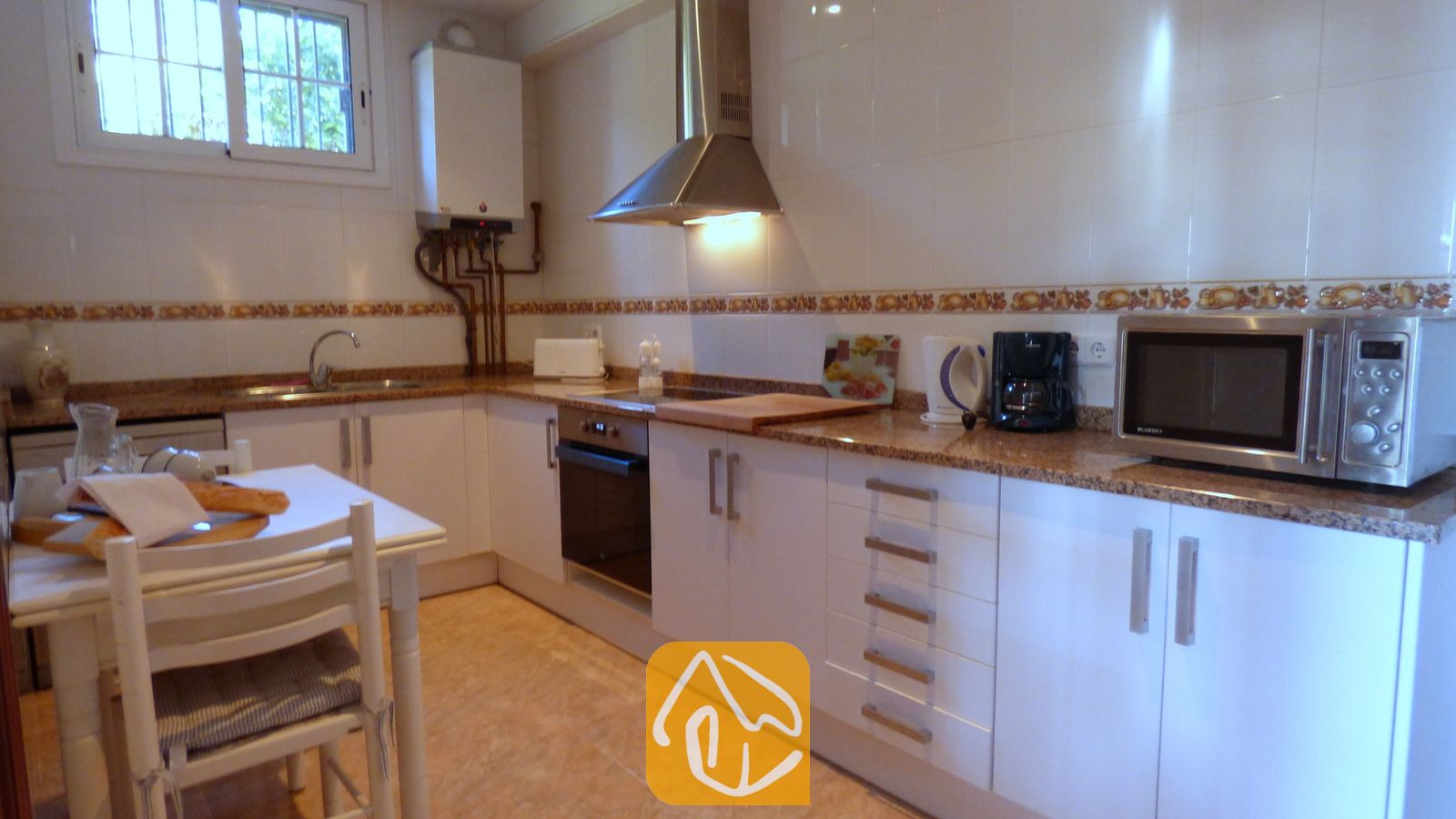 Vakantievilla's Costa Brava Spanje - Villa Noa - Interieur van de keuken met witte kasten, granieten aanrechtbladen, roestvrijstalen apparatuur en een eettafel met stoelen.