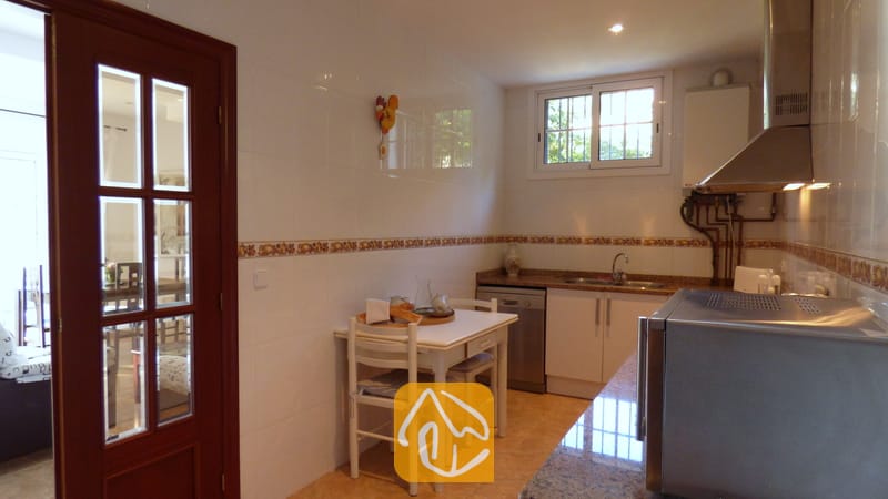 Vakantievilla's Costa Brava Spanje - Villa Noa - Keuken met witte betegelde muren, een kleine witte eettafel met twee stoelen en een donkere houten paneeldeur.