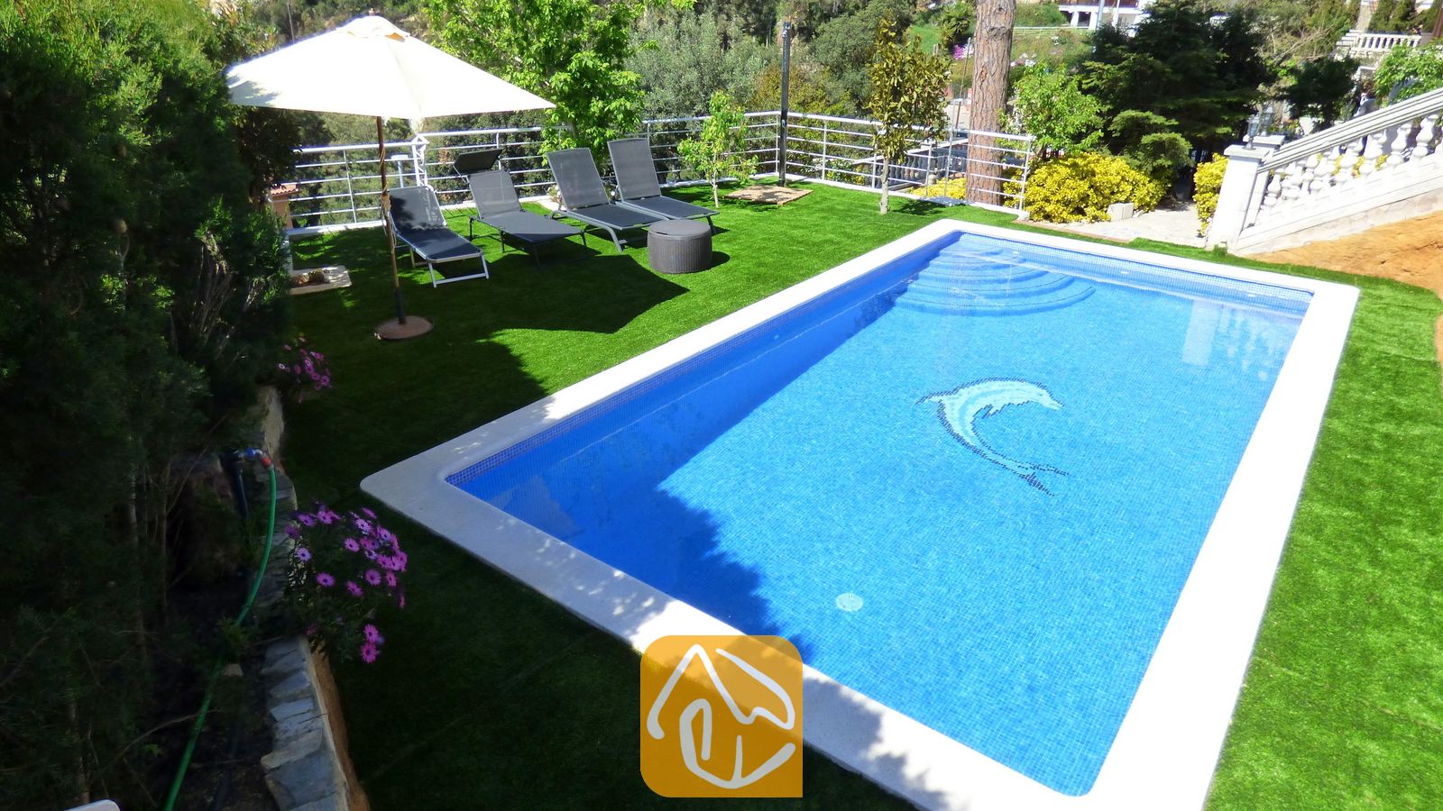 Vakantievilla's Costa Brava Spanje - Villa Noa - Privézwembad met een dolfijnmozaiëk bij Villa Noa, omringd door kunstgras, ligstoelen en een parasol.