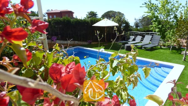 Vakantievilla's Costa Brava Spanje - Villa Noa - Het privézwembad bij Villa Noa, omlijst door rode bougainvillea, met ligstoelen en een witte parasol op het gazon op de achtergrond.