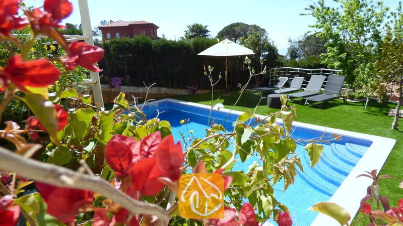 Vakantievilla's Costa Brava Spanje - Villa Noa - Het privézwembad bij Villa Noa, omlijst door rode bougainvillea, met ligstoelen en een witte parasol op het gazon op de achtergrond.