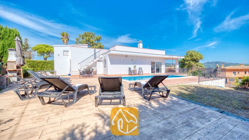 Holiday villas Costa Brava Spain - Villa Yara - Private outdoor swimming pool at Villa Yara surrounded by dark loungers on a paved terrace under a bright blue sky.