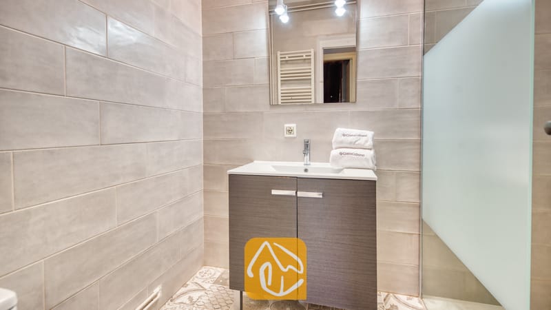 Holiday villas Costa Brava Spain - Villa Yara - Modern bathroom vanity with a white basin and folded towels underneath a rectangular mirror against grey tiled walls.