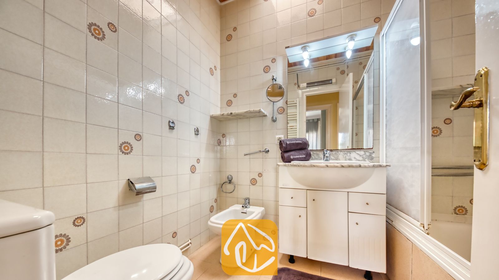 Vakantievilla's Costa Brava Spanje - Villa Yara - Betegelde badkamer voorzien van een wit badkamermeubel met wastafel, toilet, bidet en een wandspiegel met bovenverlichting.