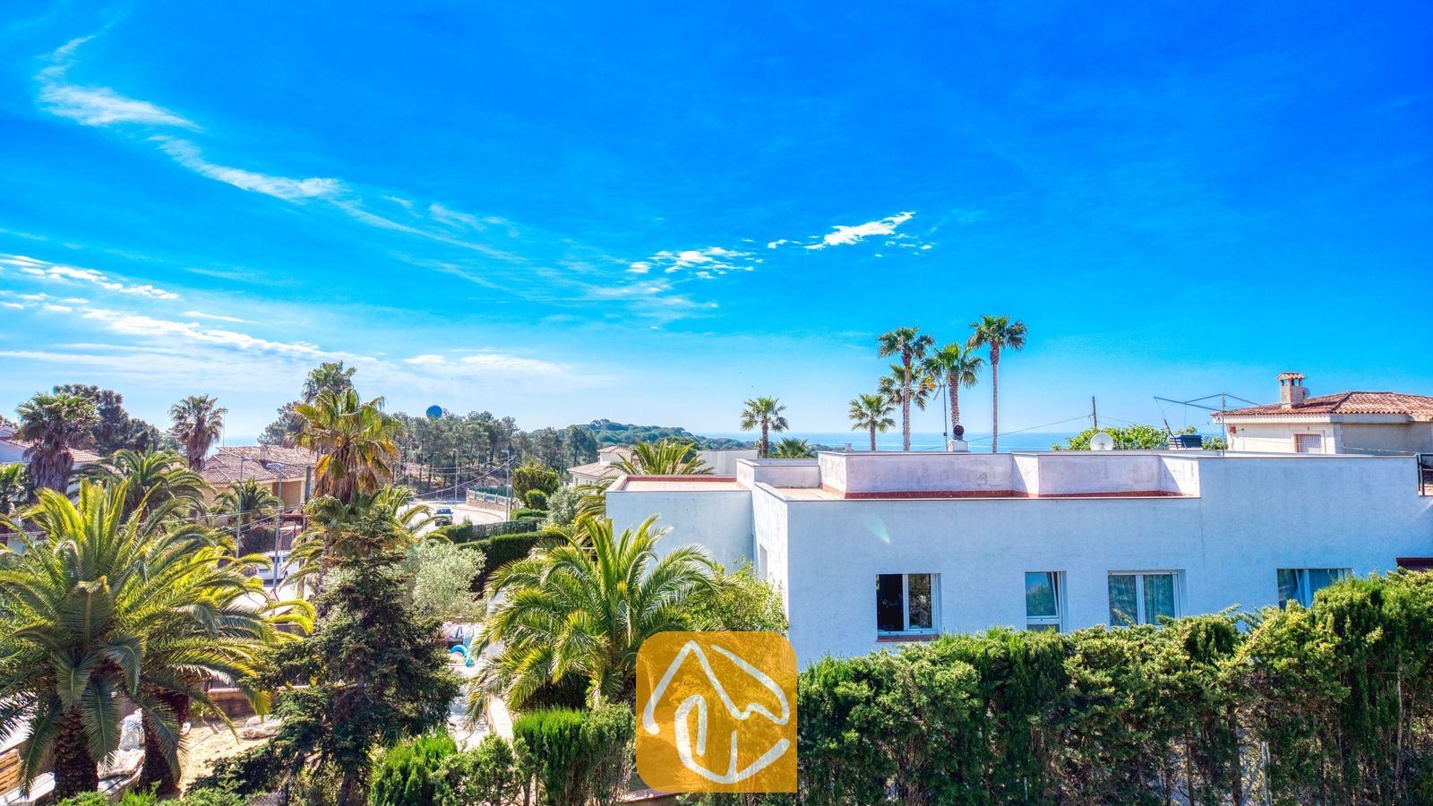 Vakantievilla's Costa Brava Spanje - Villa Yara - Buitenaanzicht van Villa Yara met witte muren, omringende palmbomen en een helderblauwe hemel.