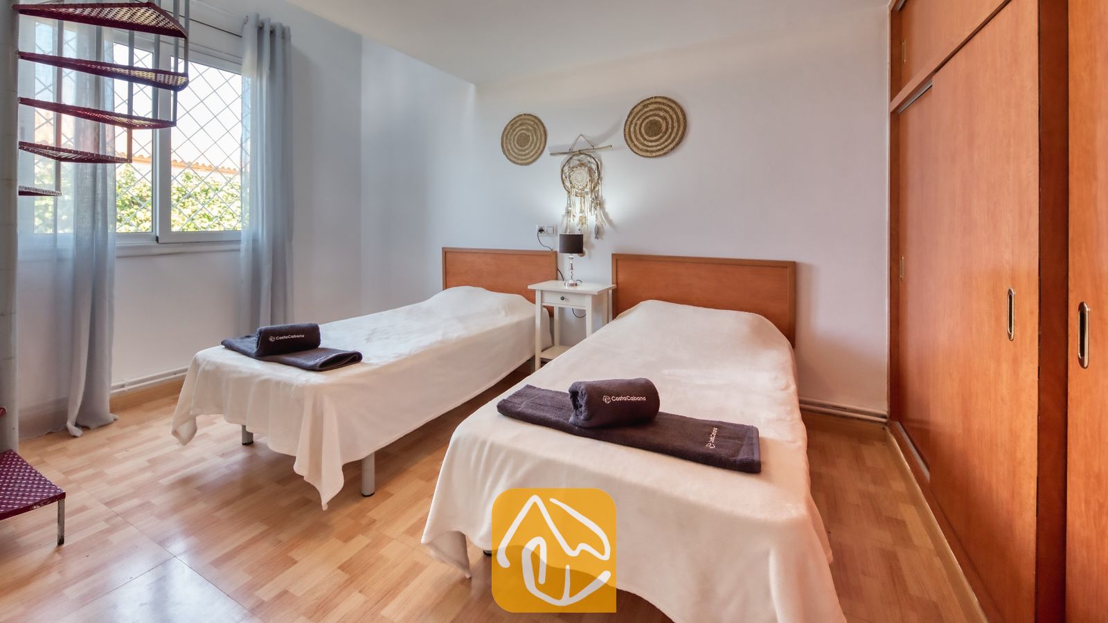 Vakantievilla's Costa Brava Spanje - Villa Yara - Slaapkamer met twee eenpersoonsbedden, voorzien van houten hoofdborden, wit beddengoed, opgerolde bruine handdoeken en een lichte houten vloer.