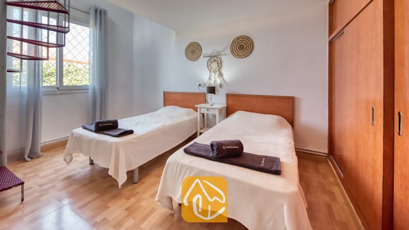 Holiday villas Costa Brava Spain - Villa Yara - Bedroom with two single beds featuring wooden headboards, white linens, rolled brown towels, and light wood flooring.