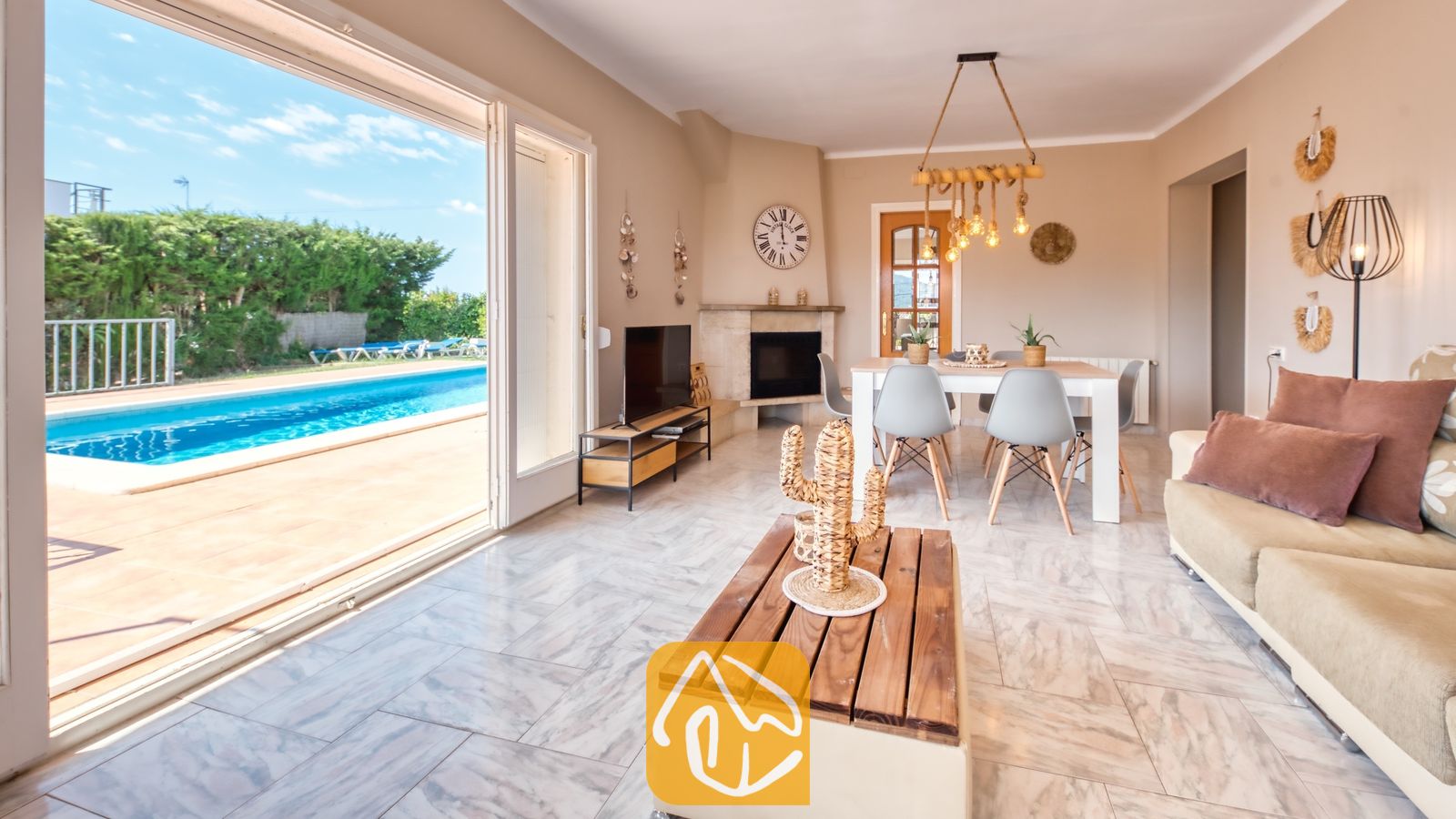 Vakantievilla's Costa Brava Spanje - Villa Yara - Woonkamer van Villa Yara met grote glazen schuifpui die uitkomt op een zwembad, een beige bank, een houten salontafel en een eethoek op de achtergrond.