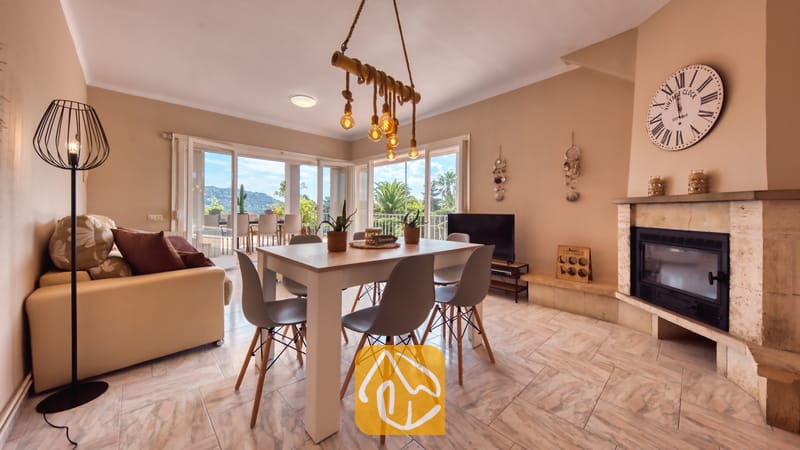 Vakantievilla's Costa Brava Spanje - Villa Yara - Woon- en eethoek in Villa Yara, voorzien van een houten eettafel met grijze stoelen, een stenen open haard en grote glazen deuren die uitkomen op een terras.