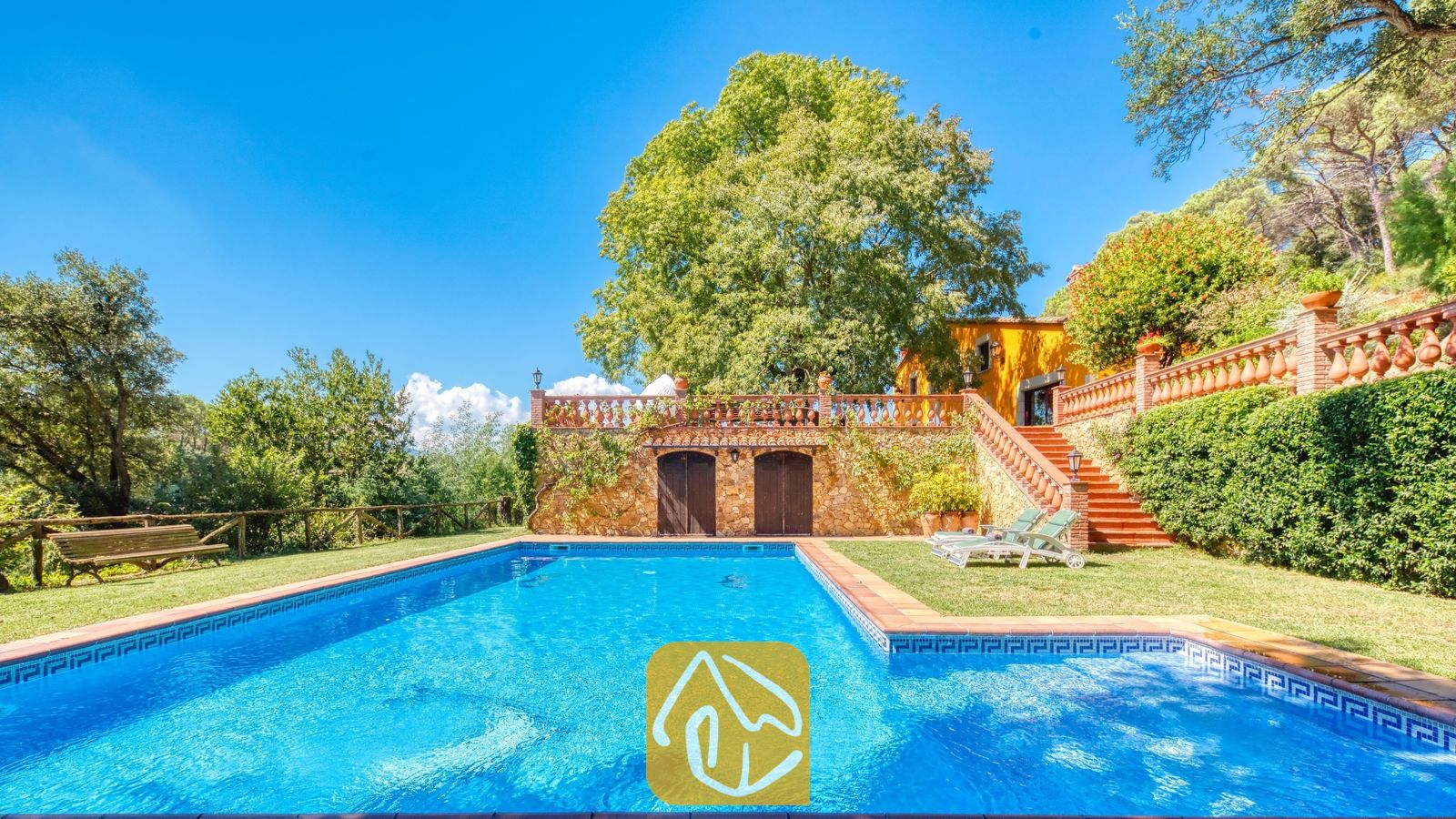 Vakantievilla's Costa Brava Spanje - Villa Paradise - Privézwembad bij Villa Paradise met helderblauw water, omringd door een groen grasveld, een stenen keermuur en comfortabele ligstoelen.