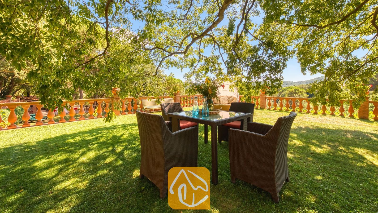Vakantievilla's Costa Brava Spanje - Villa Paradise - Tuineettafel met vier donkere rieten armstoelen op een grasgazon onder schaduwrijke bomen bij Villa Paradise