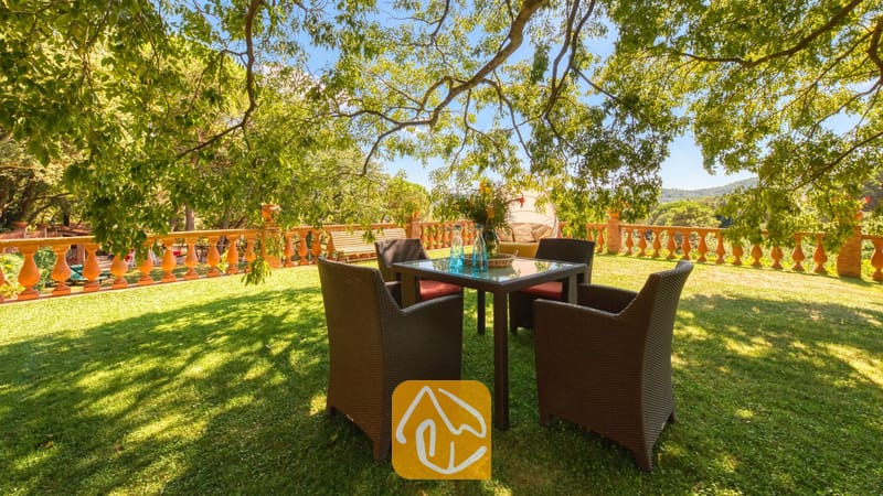 Vakantievilla's Costa Brava Spanje - Villa Paradise - Tuineettafel met vier donkere rieten armstoelen op een grasgazon onder schaduwrijke bomen bij Villa Paradise