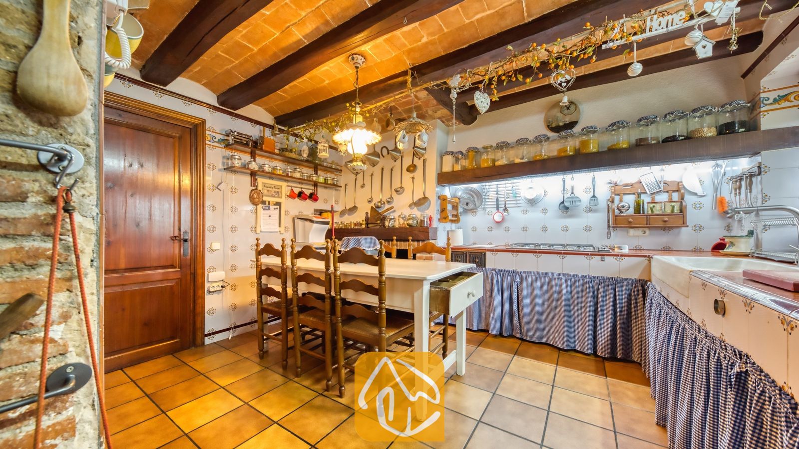 Vakantievilla's Costa Brava Spanje - Villa Paradise - Rustieke keuken met een houten eettafel, betegelde muren, zichtbare plafondbalken en blauw-wit geruite gordijnen.