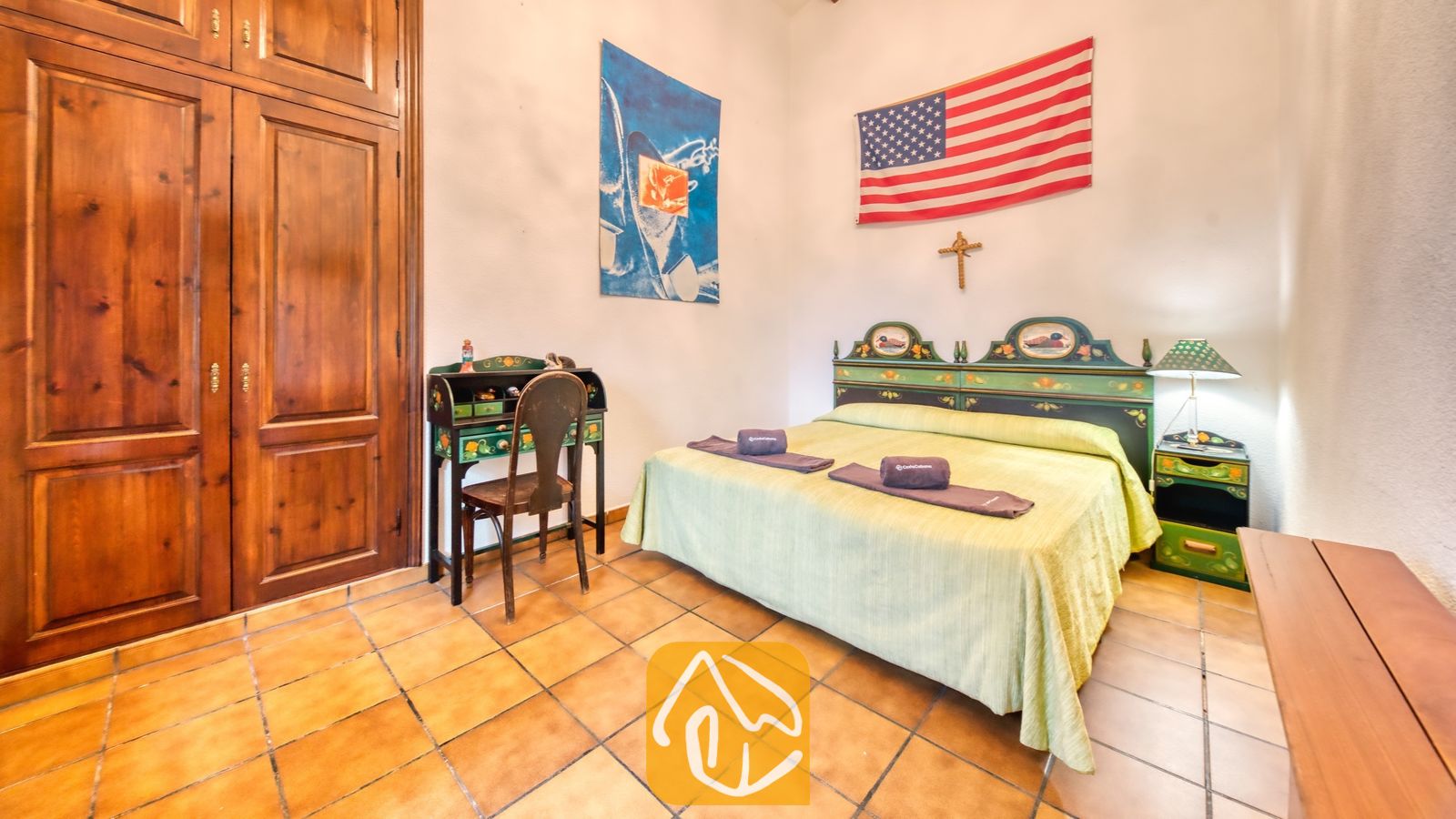 Vakantievilla's Costa Brava Spanje - Villa Paradise - Slaapkamer met een groen houten hoofdbord, een twijfelaar/tweepersoonsbed met opgevouwen handdoeken, een bijpassend groen nachtkastje met een lamp en grote houten kledingkastdeuren.