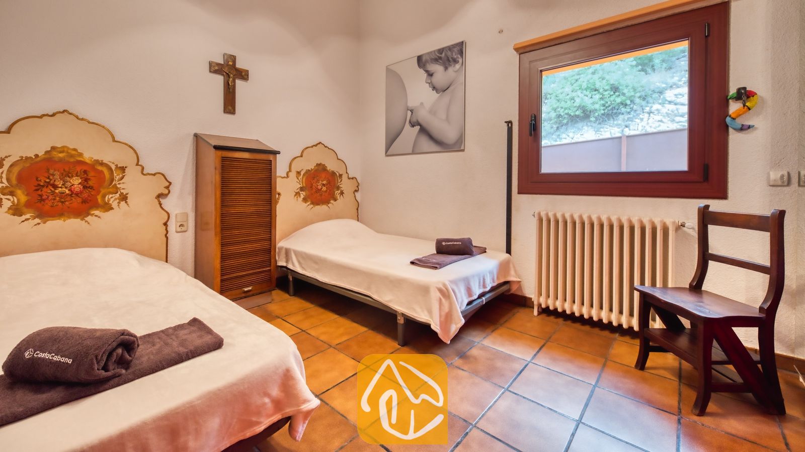 Vakantievilla's Costa Brava Spanje - Villa Paradise - Tweepersoonskamer met twee eenpersoonsbedden en fraai beschilderde hoofdborden, terracotta tegelvloeren en een donkere houten kast tussen de bedden in.
