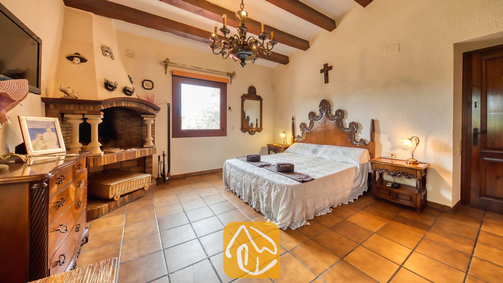 Vakantievilla's Costa Brava Spanje - Villa Paradise - Slaapkamer met houten plafondbalken, een sierlijk snijwerk hoofdeinde, tegelvloer en een bakstenen open haard in Villa Paradise.