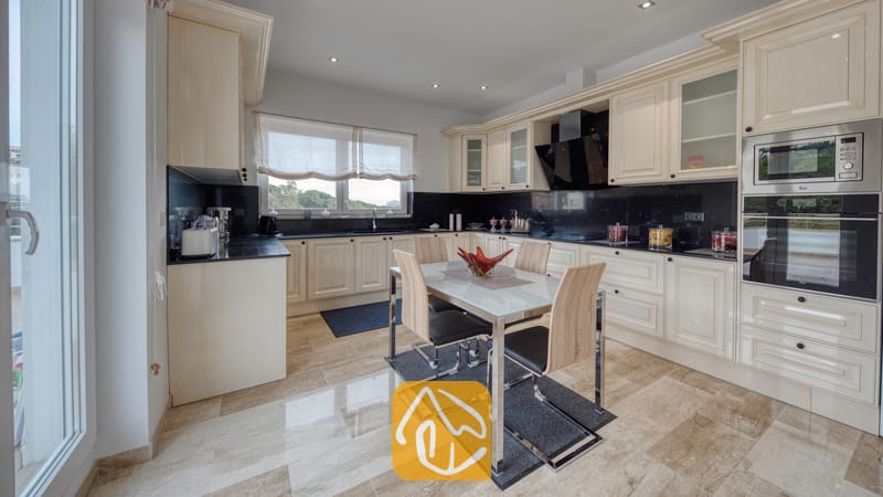 Vakantievilla's Costa Brava Spanje - Villa Madison - Moderne keuken met crèmekleurige kasten, zwarte granieten aanrechtbladen en een eettafel met vier stoelen bij Villa Madison.