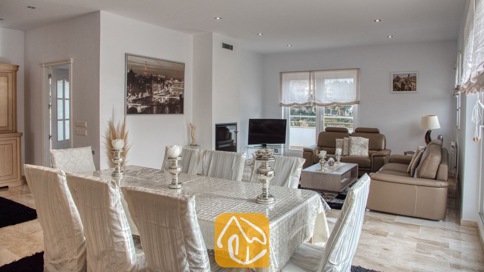 Vakantievilla's Costa Brava Spanje - Villa Madison - Woon- en eetkamer in Villa Madison, voorzien van een grote eettafel met een witte hoes, zilveren kandelaars en lichte, ﴾taan﴿ lederen banken.