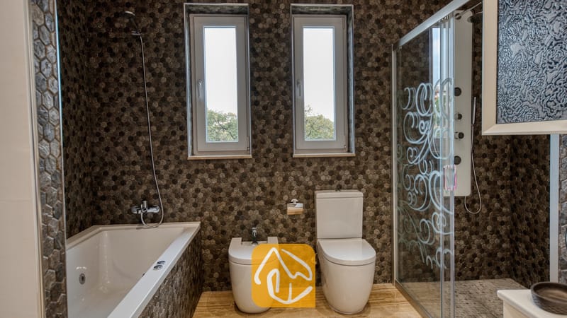 Holiday villas Costa Brava Spain - Villa Madison - Modern bathroom featuring brown hexagonal tiled walls, a white bathtub, toilet, bidet, and a separate glass-door shower enclosure.