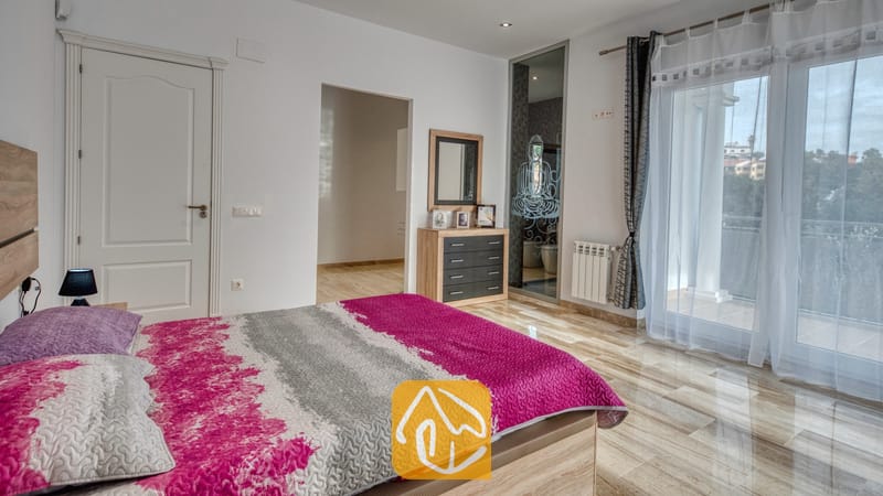 Vakantievilla's Costa Brava Spanje - Villa Madison - Slaapkamer in Villa Madison met een bed met roze en grijs geprint sprebed, gepolijste tegelvloeren en glazen balkondeuren.