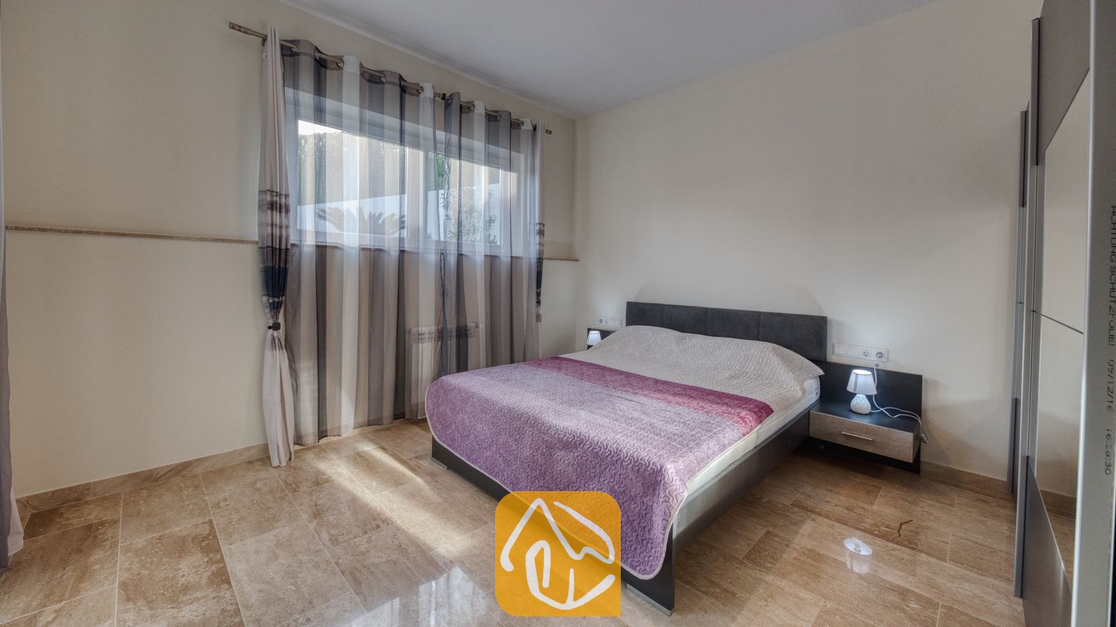 Vakantievilla's Costa Brava Spanje - Villa Madison - Slaapkamer met een tweepersoonsbed voorzien van een paars geprint sprei, doorschijnende gestreepte gordijnen voor het raam en gepolijste marmeren tegelvloeren.