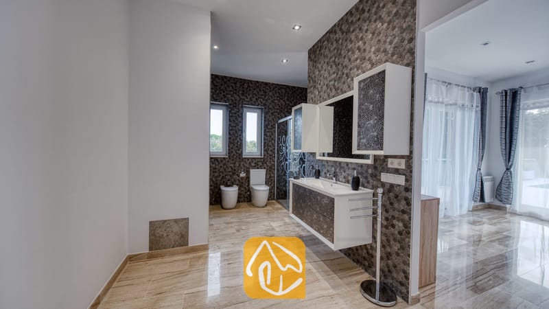 Vakantievilla's Costa Brava Spanje - Villa Madison - Moderne badkamer met donkere honingraatmozaïektegels, een zwevend wit badkamermeubel met gedessineerde kastdeuren en gepolijste marmeren vloeren.