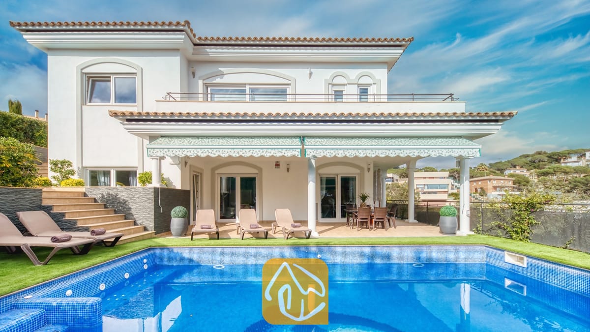 Vakantievilla's Costa Brava Spanje - Villa Madison - Buitenaanzicht van Villa Madison met een blauw betegeld zwembad, ligstoelen en een overdekt terras met witte zuilen tegen een helderblauwe hemel