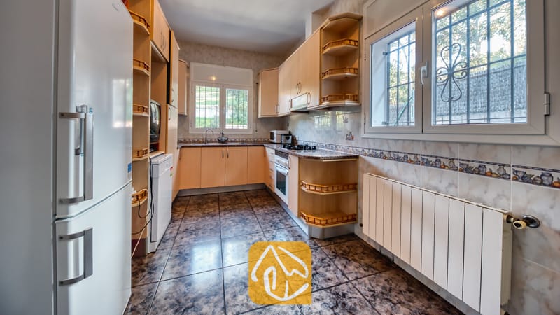 Vakantievilla's Costa Brava Spanje - Villa Zarita - Keuken met lichte houten kasten, donkere patroonvloertegels en links een witte koelkast