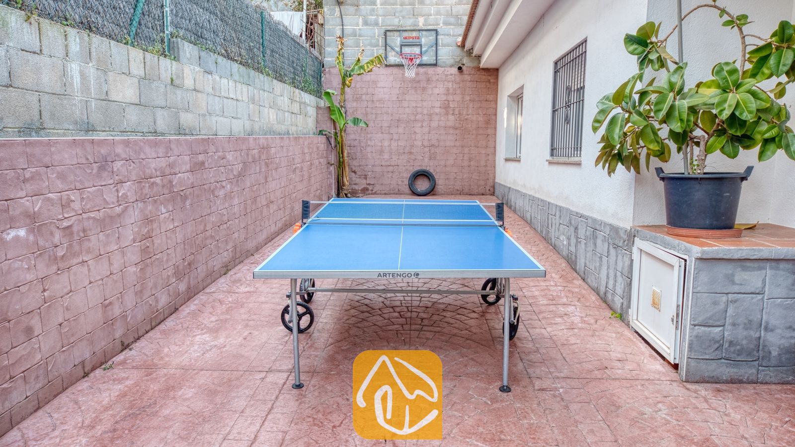 Vakantievilla's Costa Brava Spanje - Villa Zarita - Binnenplaats van Villa Zarita met een blauwe tafeltennistafel op een roodachtig aaneengesloten terras en een basketbalring aan de achtermuur.