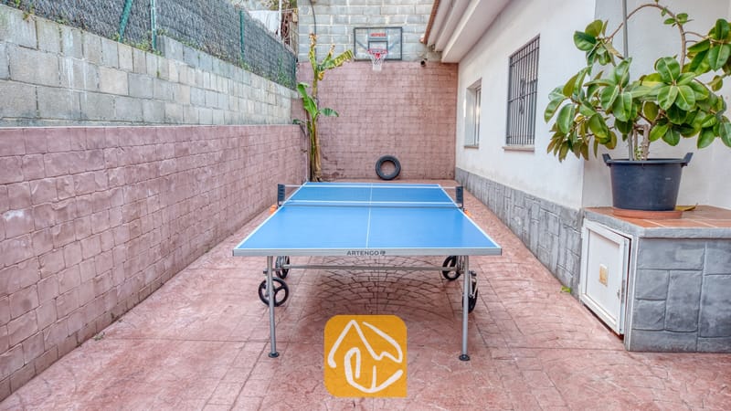 Holiday villas Costa Brava Spain - Villa Zarita - Outdoor courtyard at Villa Zarita featuring a blue table tennis table on a reddish paved patio with a basketball hoop on the back wall.