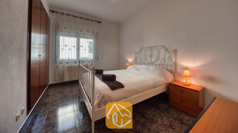Vakantievilla's Costa Brava Spanje - Villa Zarita - Slaapkamer met een wit metalen bed, donkere tegelvloer, houten nachtkastje met een oranje lamp en een inbouwkast.