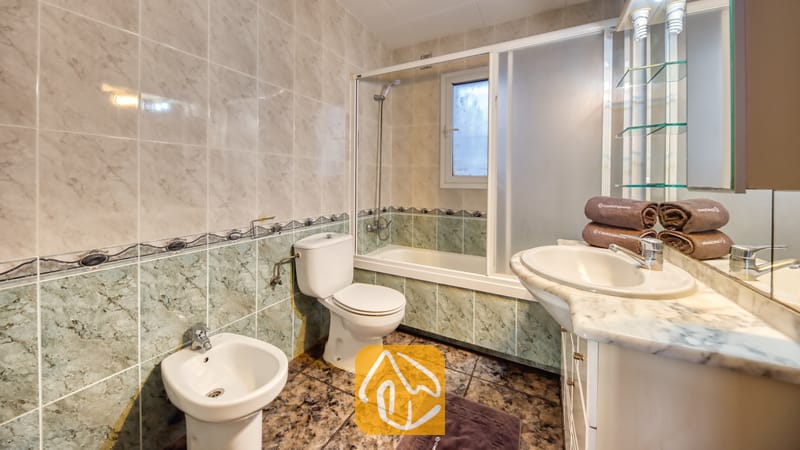 Holiday villas Costa Brava Spain - Villa Zarita - Bathroom featuring marbled tile walls, a white vanity with a countertop sink, a toilet, a bidet, and a bathtub with sliding glass doors.