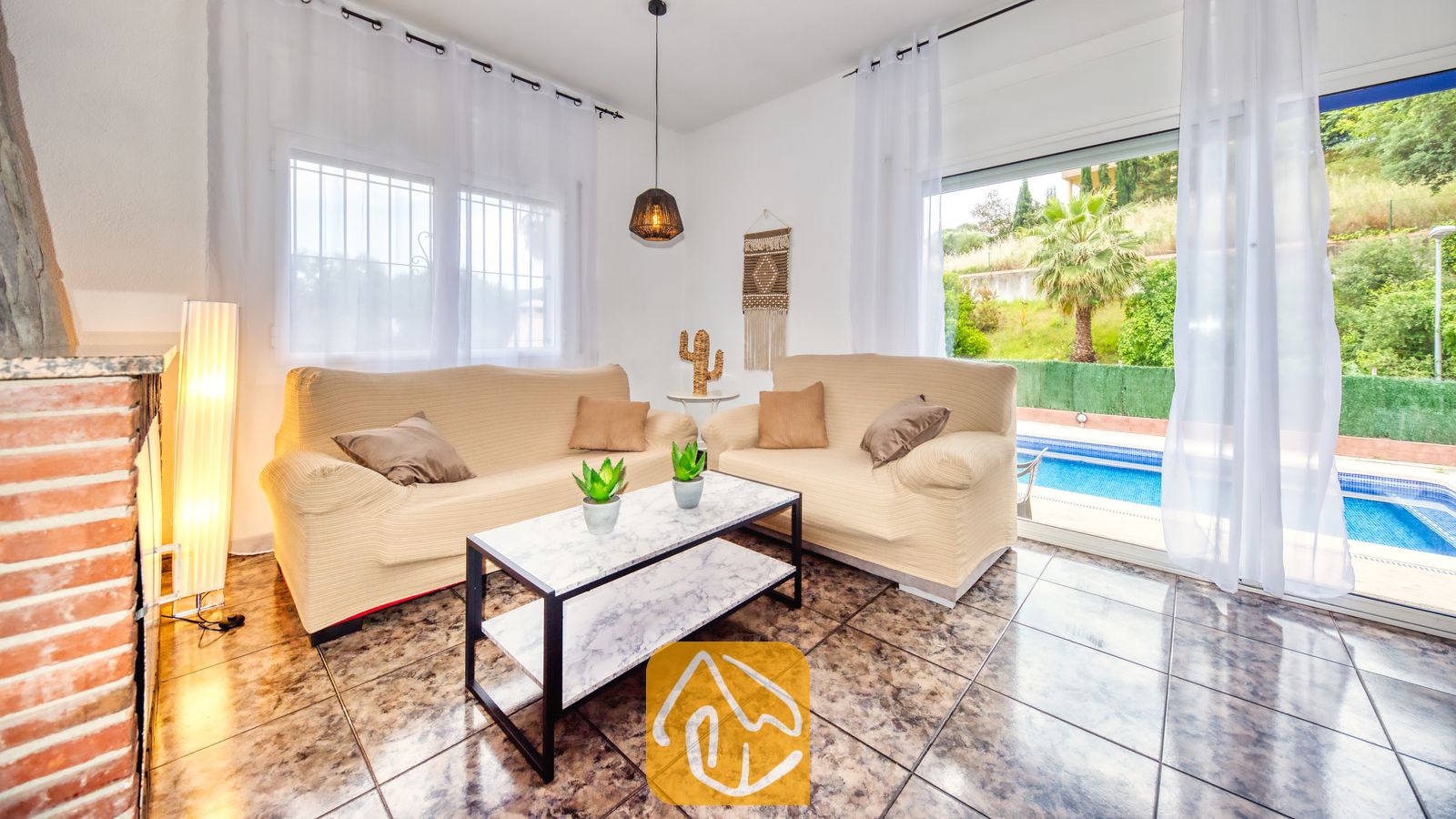 Vakantievilla's Costa Brava Spanje - Villa Zarita - Woonkamer van Villa Zarita met twee beige banken, een salontafel met marmeren blad en glazen schuifpuien die uitkomen op een zwembad.