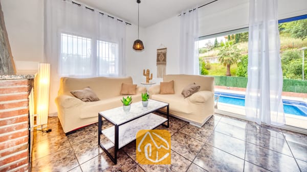 Vakantievilla's Costa Brava Spanje - Villa Zarita - Woonkamer van Villa Zarita met twee beige banken, een salontafel met marmeren blad en glazen schuifpuien die uitkomen op een zwembad.