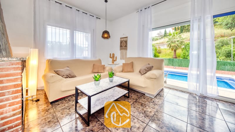 Vakantievilla's Costa Brava Spanje - Villa Zarita - Woonkamer van Villa Zarita met twee beige banken, een salontafel met marmeren blad en glazen schuifpuien die uitkomen op een zwembad.