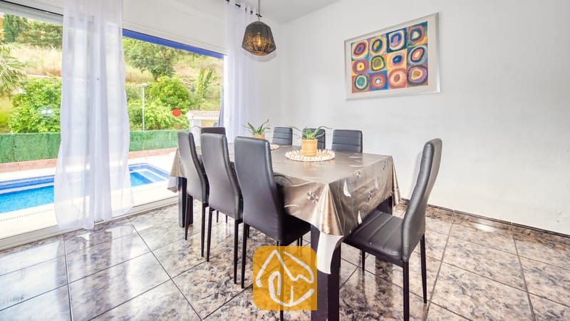 Vakantievilla's Costa Brava Spanje - Villa Zarita - Eetgedeelte in Villa Zarita met een donkere tafel, zwartlederen stoelen, abstracte wanddecoratie en glazen schuifpuien die uitkomen op een zwembadterras.