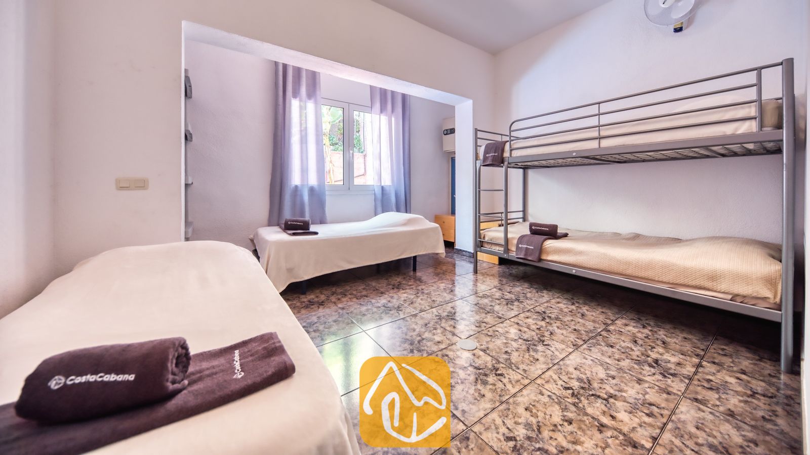 Vakantievilla's Costa Brava Spanje - Villa Zarita - Slaapkamer met metalen stapelbedden, eenpersoonsbedden met wit beddengoed, bruine handdoeken, tegelvloeren en een raam met in-betweens.