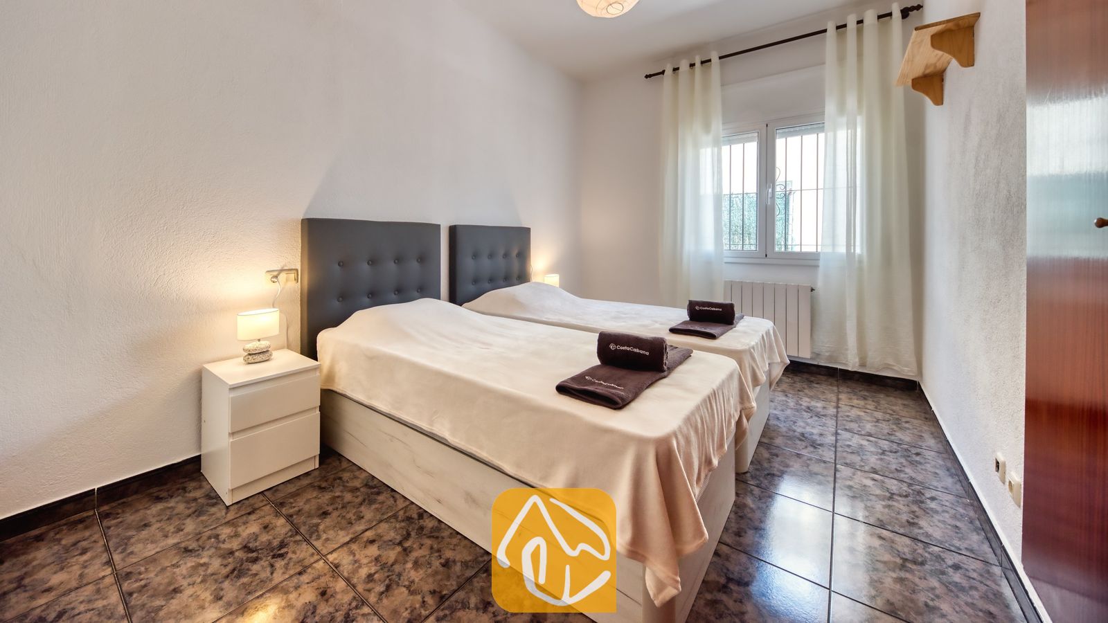 Vakantievilla's Costa Brava Spanje - Villa Zarita - Slaapkamer met twee eenpersoonsbedden, voorzien van donkere gecapitonneerde hoofdborden, lichtbeige spreien en opgevouwen donkere handdoeken bij Villa Zarita.