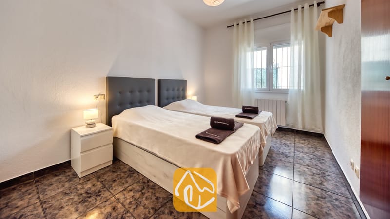 Vakantievilla's Costa Brava Spanje - Villa Zarita - Slaapkamer met twee eenpersoonsbedden, voorzien van donkere gecapitonneerde hoofdborden, lichtbeige spreien en opgevouwen donkere handdoeken bij Villa Zarita.
