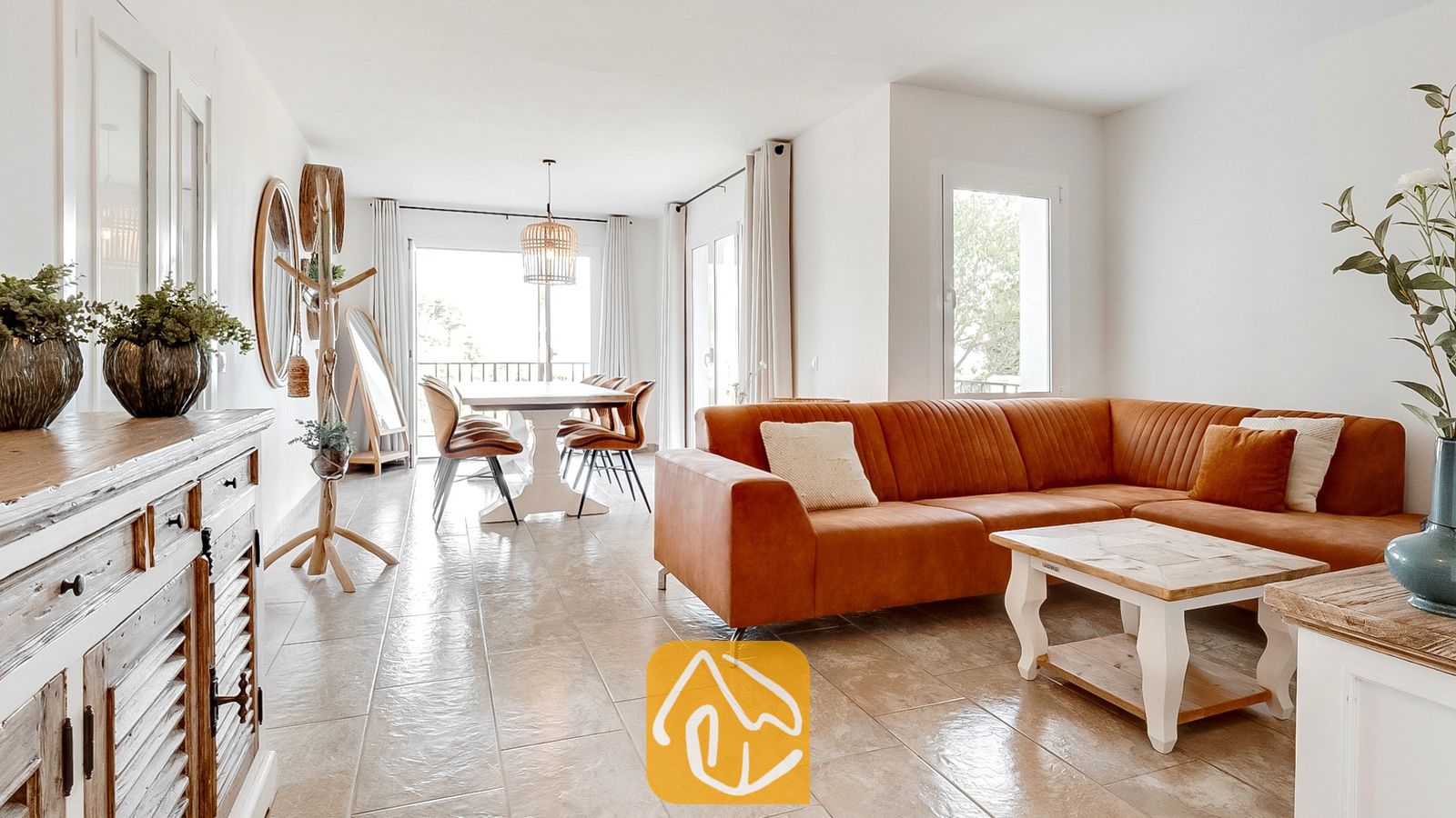 Vakantievilla's Costa Brava Spanje - Villa Tropicana - Lichte woonkamer in Villa Tropicana, voorzien van een grote roestbruine hoekbank, een houten salontafel en plavuizen vloeren die overlopen in een eethoek.