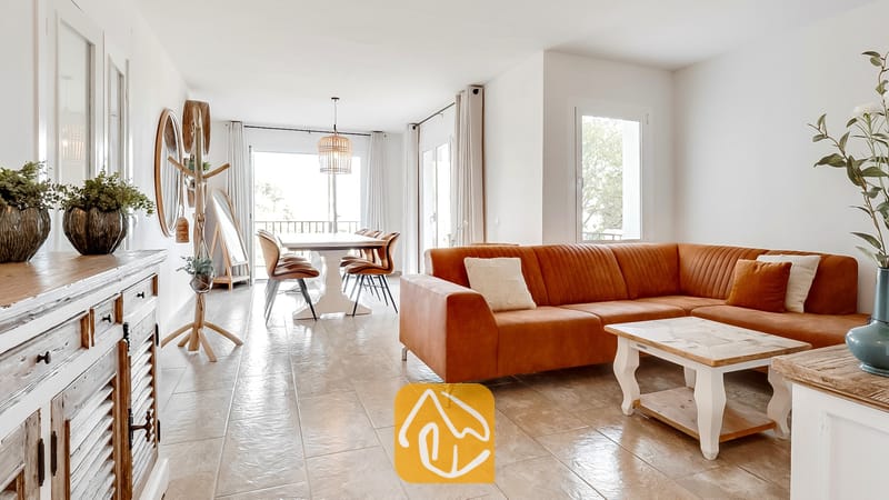 Vakantievilla's Costa Brava Spanje - Villa Tropicana - Lichte woonkamer in Villa Tropicana, voorzien van een grote roestbruine hoekbank, een houten salontafel en plavuizen vloeren die overlopen in een eethoek.