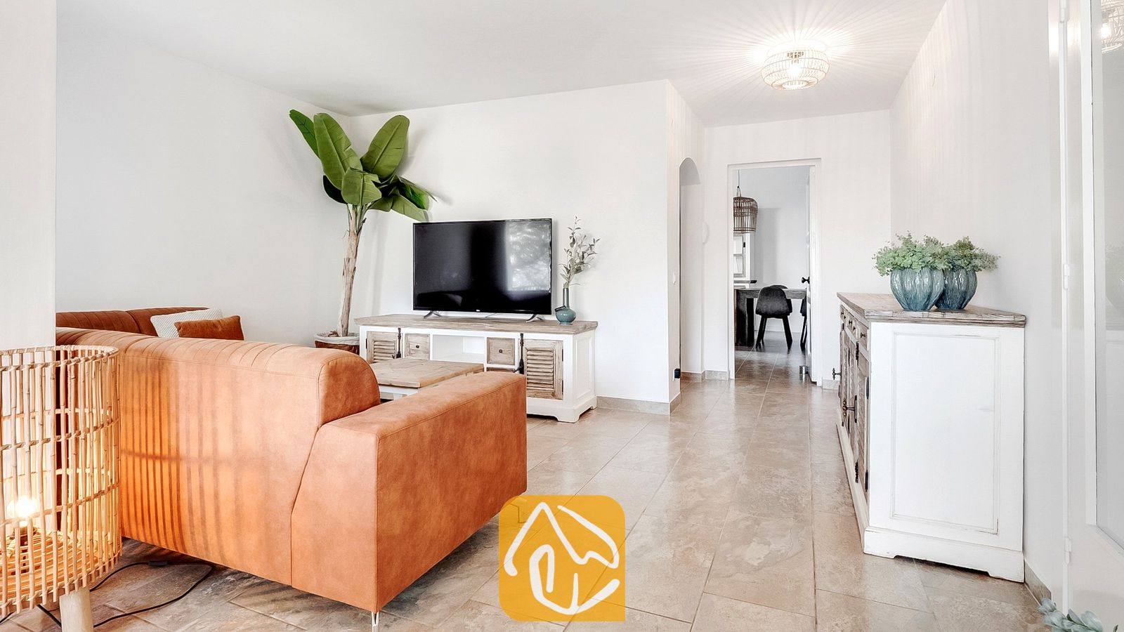 Vakantievilla's Costa Brava Spanje - Villa Tropicana - Woonkamer van Villa Tropicana met een bruine leren bank, flatscreen-televisie op een rustiek wit tv-meubel en tegelvloeren.