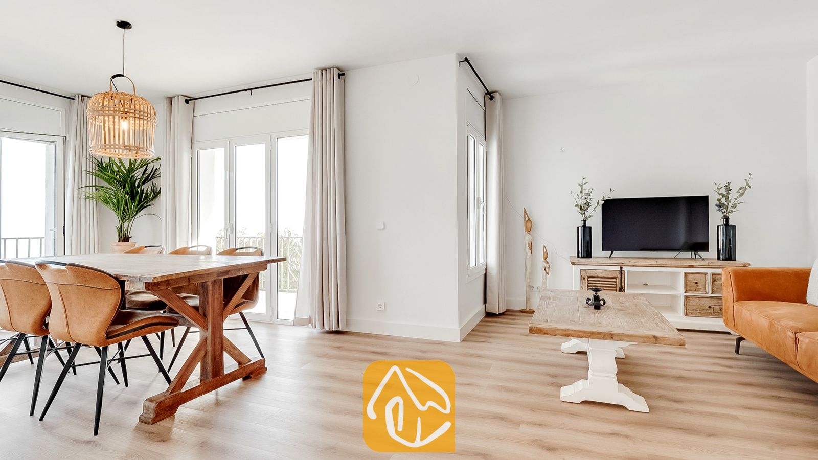 Vakantievilla's Costa Brava Spanje - Villa Tropicana - Ruime woon- en eetkamer in Villa Tropicana, voorzien van een houten eettafel, cognakleurige lederen stoelen, een licht houten vloer en grote glazen deuren met neutrale gordijnen.
