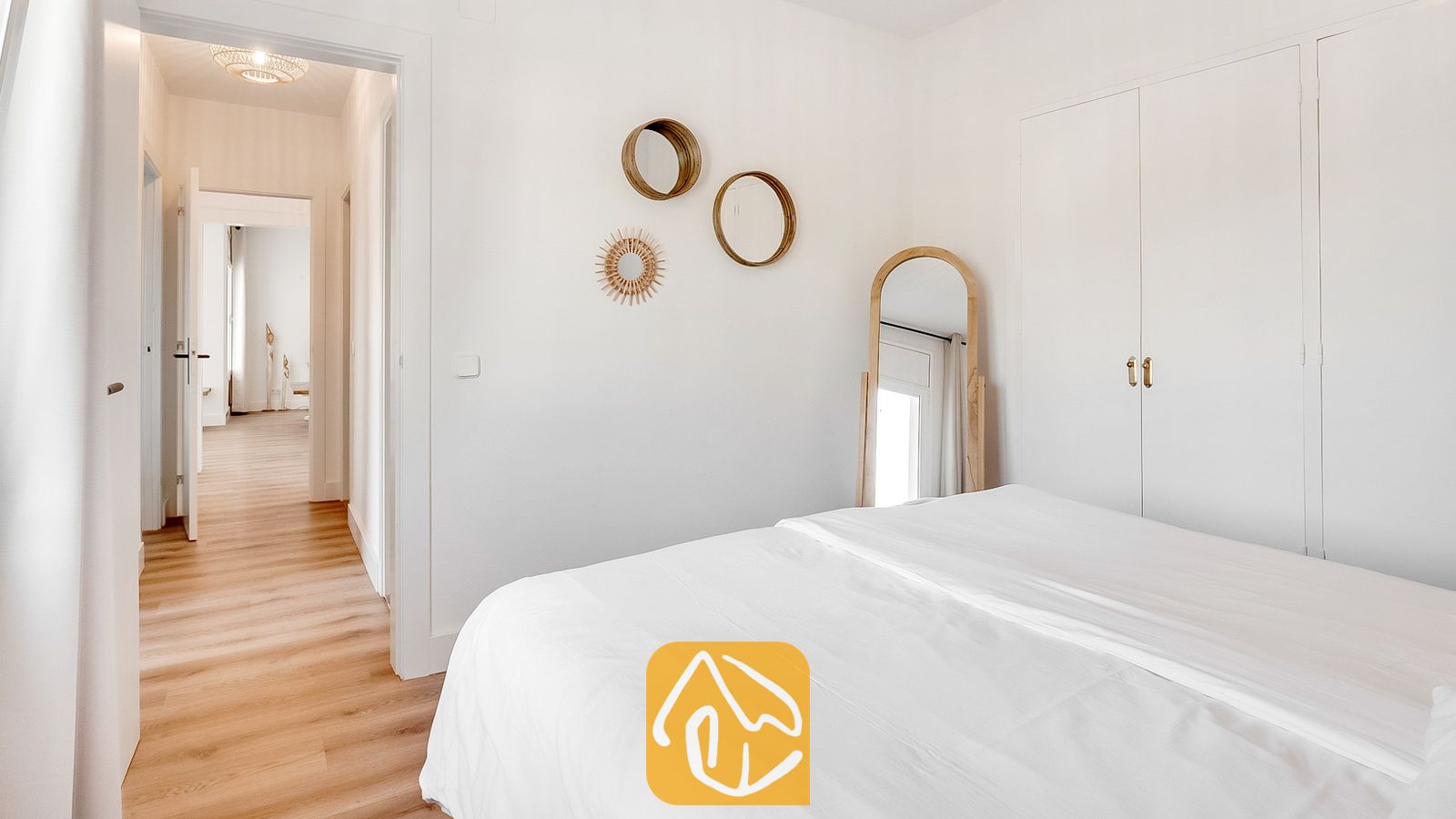 Vakantievilla's Costa Brava Spanje - Villa Tropicana - Slaapkamer met een wit bed, houten vloeren, ronde wandspiegels en een boogvormige spiegel van vloer tot plafond.