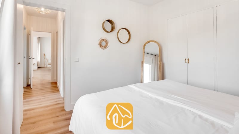 Vakantievilla's Costa Brava Spanje - Villa Tropicana - Slaapkamer met een wit bed, houten vloeren, ronde wandspiegels en een boogvormige spiegel van vloer tot plafond.