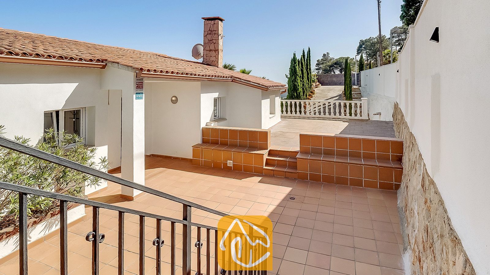 Vakantievilla's Costa Brava Spanje - Villa Tropicana - Buitenterras van Villa Tropicana met plavuizen, aanzittende keramische banken en een stenen open haard onder een helderblauwe hemel