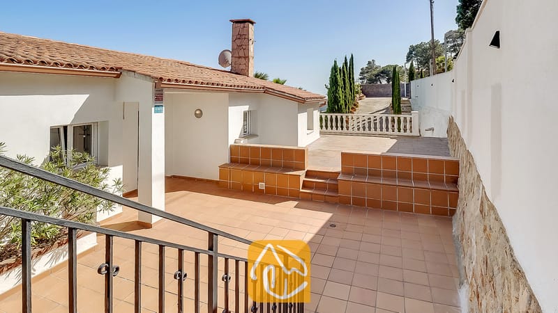 Vakantievilla's Costa Brava Spanje - Villa Tropicana - Buitenterras van Villa Tropicana met plavuizen, aanzittende keramische banken en een stenen open haard onder een helderblauwe hemel
