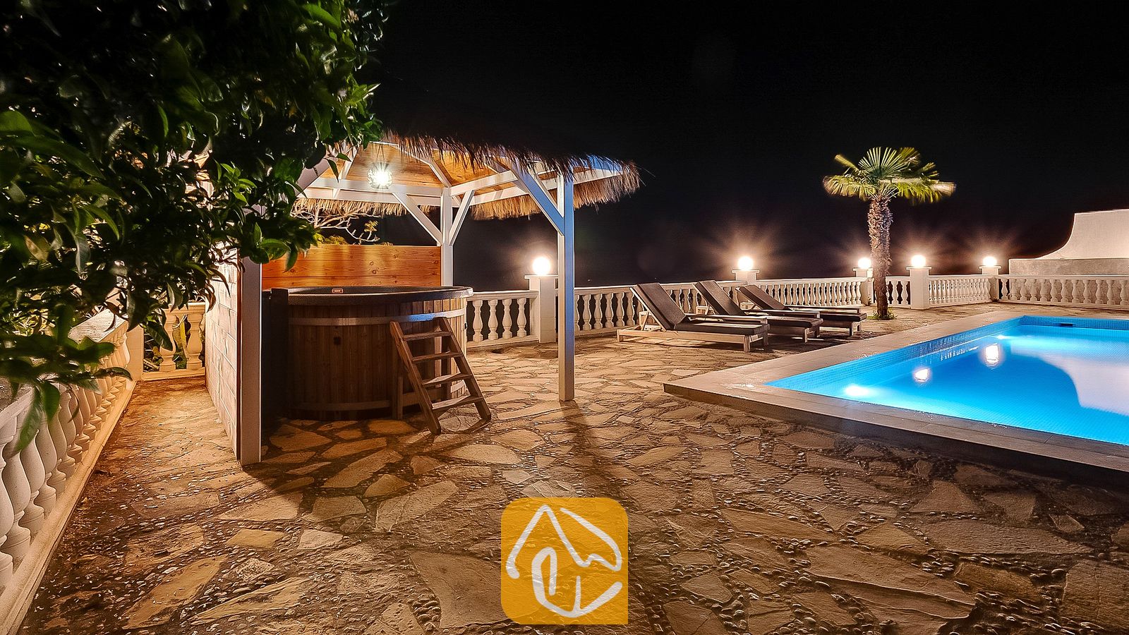 Vakantievilla's Costa Brava Spanje - Villa Tropicana - Verlicht zwembad en houten hottub onder een rieten gazebo op het stenen terras van Villa Tropicana bij nacht.