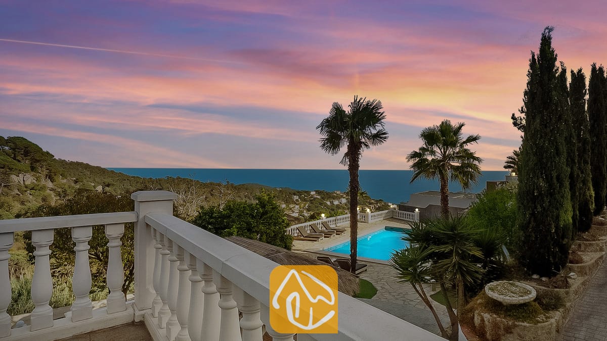 Vakantievilla's Costa Brava Spanje - Villa Tropicana - Terras met uitzicht op Villa Tropicana, voorzien van een eigen zwembad, palmbomen en zeezicht onder een roze en blauwe zonsondergang.